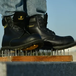 Black VITOSAFE safety boots standing directly on a wooden board full of nails, demonstrating excellent puncture-resistant and anti-smash protection.